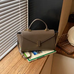 Elegant taupe textured leather handbag featuring a gold clasp on a wooden window sill