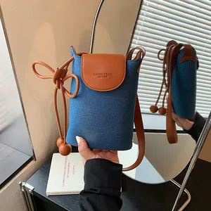 Detailed view of stylish denim and brown leather crossbody phone bag with decorative charms