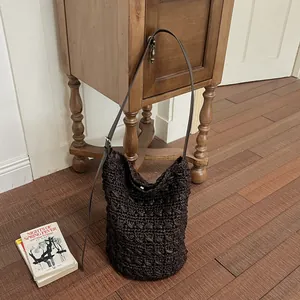 Detailansicht einer dunkelbraunen handgefertigten Strohtasche mit schmalem Lederriemen