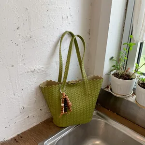 Detailed view of a green woven bucket bag with unique wooden bead charm on a strap.