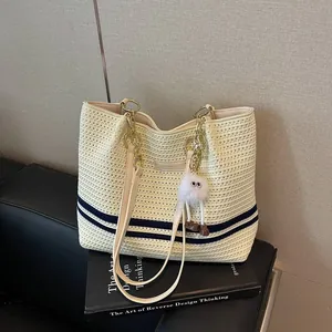Cream woven tote bag with blue stripes and a white fuzzy monster charm accessory.