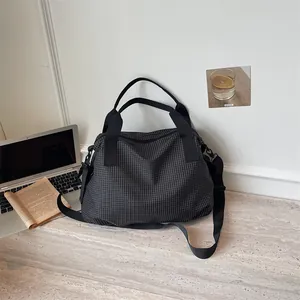 Grande borsa da viaggio a scacchi esposta con un laptop e un libro in un ambiente moderno.