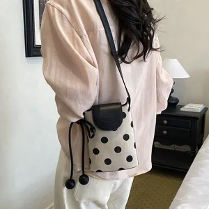 Detail view of a stylish polka dot crossbody phone bag worn by a model in a cozy room