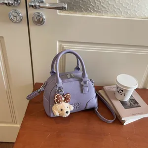 Detail view of a stylish purple textured Boston bag with a cute dog plush charm