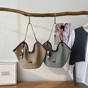 Hand-woven straw tote bags in brown and grey hanging with decorative bead charms.