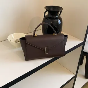 Detail of a brown crossgrain leather handbag with elegant gold clasp and top handle.