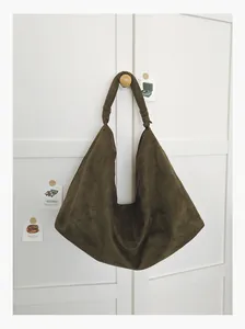 Detail view of a vintage olive green suede hobo bag hanging on a white cabinet door.