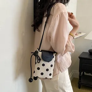 Close-up view of a chic polka dot canvas phone bag styled on a female model's shoulder