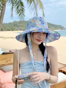 Frau mit stilvollem blauem Blumen-Anglerhut mit breiter Krempe und langen Bändern am Strand