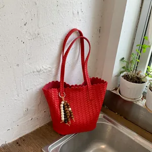 Red woven bucket bag with beaded tassel in a minimalist indoor lifestyle setting.