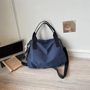 Grande borsa da viaggio a scacchi blu su una scrivania con laptop e libro in dettaglio