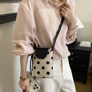 Lifestyle shot featuring a woman wearing a chic cream and black polka dot crossbody phone bag