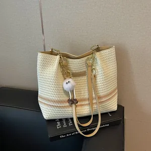 Close-up detail of a woven striped tote bag featuring elegant gold chain straps and a charm