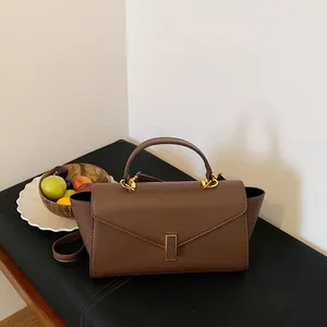 Elegant brown leather top-handle handbag with gold clasp on black display bench with fruits