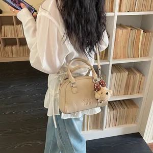 Detailed view of a stylish beige leather Boston bag featuring a cute bear charm and strap