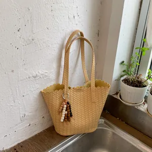 Close-up of a woven beige bucket bag with a wavy rim and colorful bead tassel charm