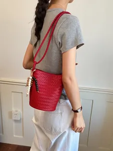 Rote geflochtene Eimertasche für Sommermode mit verstellbarem Riemen und Anhängern.