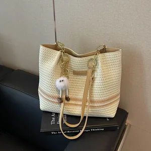 Detailed view of cream woven tote bag with gold chain straps and a fuzzy monster charm.