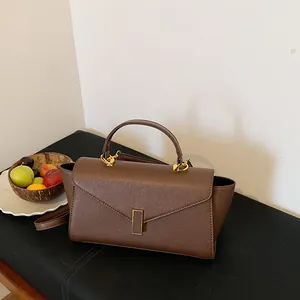 Close-up of a brown Saffiano leather handbag with gold clasp on a display surface.