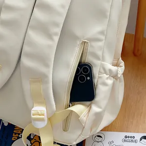 Detail view of cream white backpack with side zipper pocket holding a smartphone on wood table