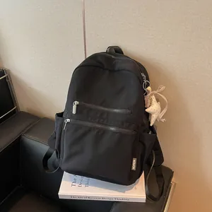 Detalle de una mochila negra minimalista apoyada sobre un libro de diseño blanco.