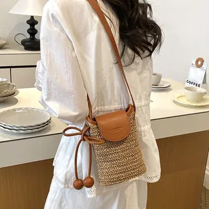 Detailed close-up view of a straw woven crossbody phone bag with leather flap and bow decoration