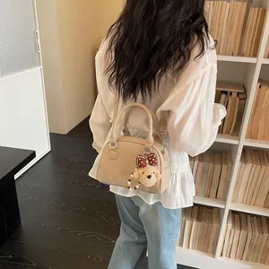 Detailed back view of a chic beige commuter Boston handbag featuring a cute bear charm