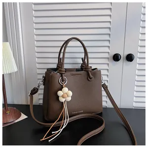 Elegante bolso bandolera de cuero granulado marrón con colgante de flor en una habitación