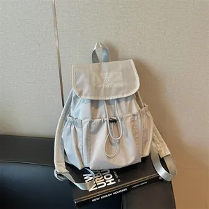 Light gray drawstring backpack with pleated texture and top flap shown in a modern interior