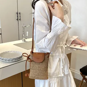 Detail view of a woven crossbody straw phone bag for women in a white dress context.