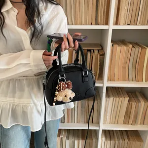 Detail view of black Boston handbag with a cute bear keychain charm in a library setting.
