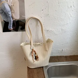 Stylish cream woven bucket bag featuring scalloped edges and a decorative beaded charm tassel