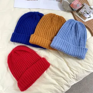 Detailed view of four colorful chunky knit beanie hats on a soft textured background.
