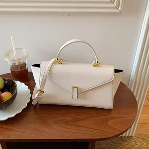 Elegant cream white structured handbag with top handle and gold clasp on a wooden table