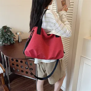 Grande borsa da viaggio a scacchi rossi indossata da una modella in un contesto lifestyle