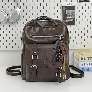 Close-up detail of brown vintage leather backpack featuring dog charm and buckled pockets