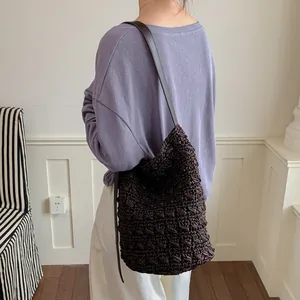 Rückansicht eines Models mit einer dunkelbraunen gewebten Stroh-Eimertasche mit Gurt.