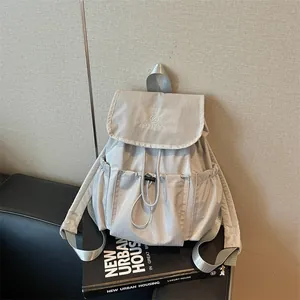 Detail view of a light grey drawstring backpack with pleated pockets and grid pattern