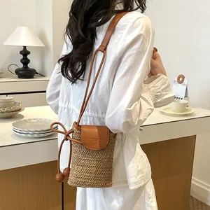 Back view detail of a woven straw crossbody phone bag with leather flap and drawstring strap