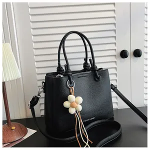 Primer plano detallado del bolso negro con textura, colgante de flor y correa para el hombro