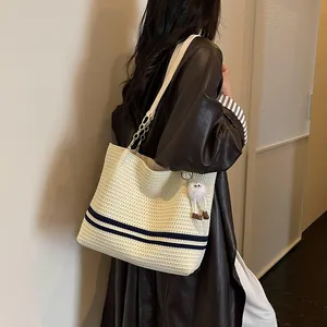 Stylish cream woven tote bag with navy stripes worn over a dark brown leather coat