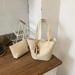 Beige woven bucket bag with matching clutch and decorative bead tassel in home setting