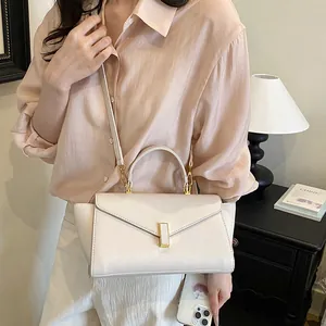 Elegant white structured handbag with gold clasp detail, carried by a model in a chic shirt.