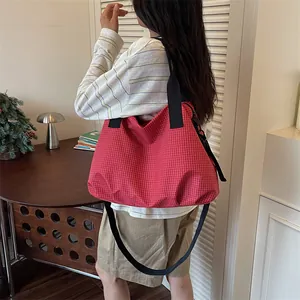 Grande borsa da viaggio a scacchi rossi indossata a spalla da una modella in casa