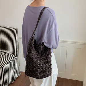 Minimalistische dunkelbraune Stroh-Eimertasche mit Lederriemen in Lifestyle-Ansicht