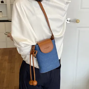 Close-up of a stylish blue denim crossbody phone bag with a textured leather flap