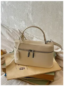 Elegant beige vanity box handbag placed on vintage books, highlighting the leather finish