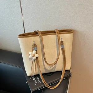 Large beige woven tote bag detail with brown leather trim and white flower charm.