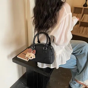 Close-up of a black Boston bag with a cute plush dog charm being carried by a woman