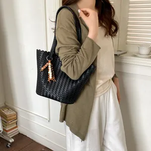 Detail showing a large black woven leather bucket bag with wooden beads decoration